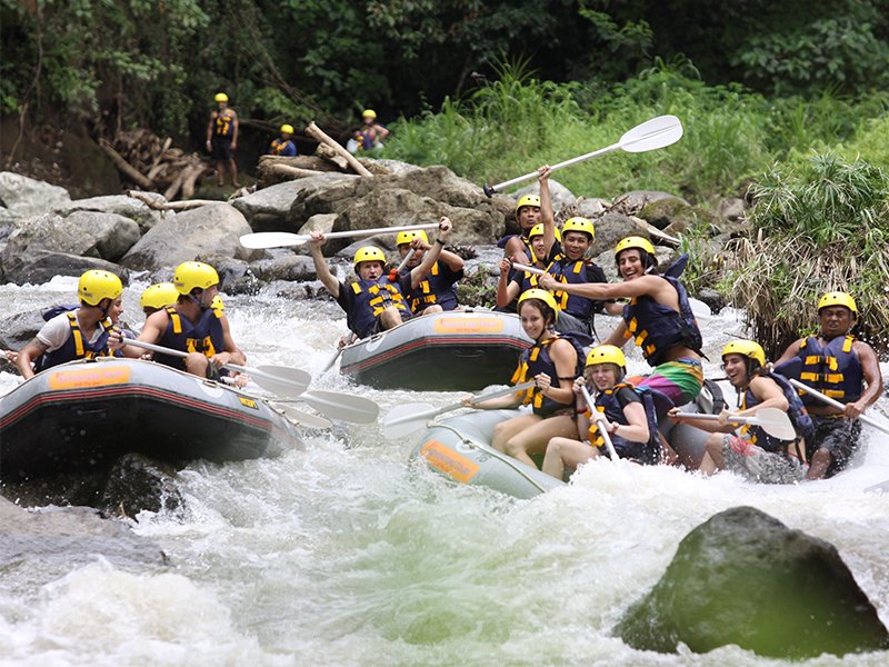 Rafters in a grey boat paddling through grade 2 rapids on the scenic Ayung River in Ubud, Bali.
