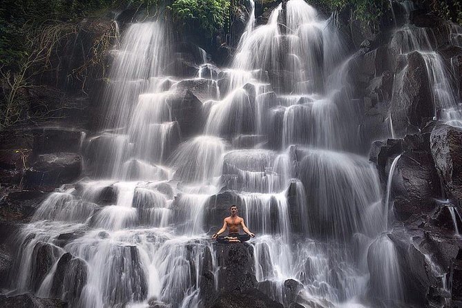 A dramatic, tiered rock cliff waterfall cascading over multiple levels at Kanto Lampo near Ubud.
