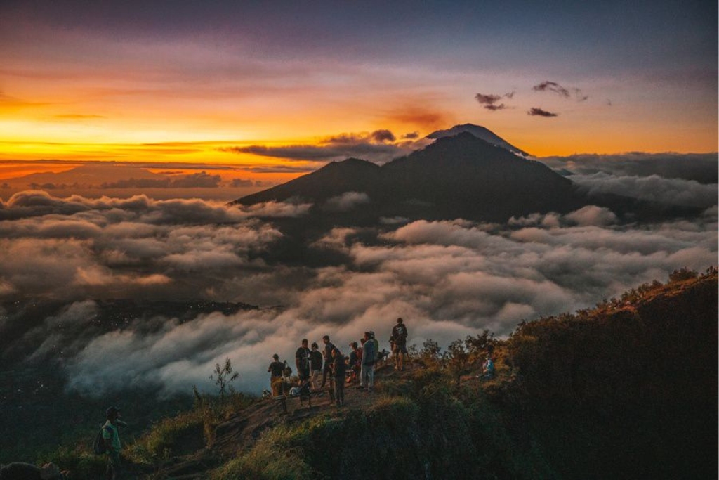Hikers standing on the summit of Mount Batur watching a golden sunrise over the clouds in Bali.