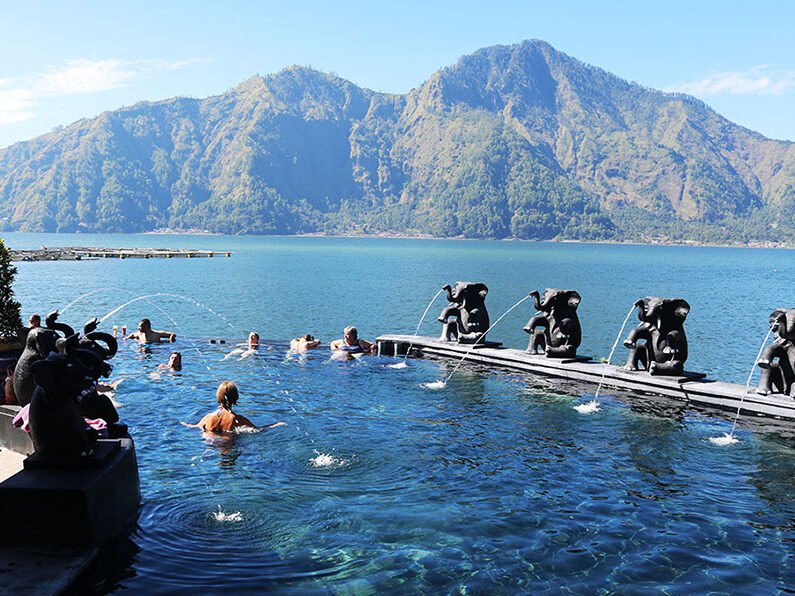 Tourists relaxing in a natural hot spring pool with a view of the Mount Batur volcano in Kintamani.