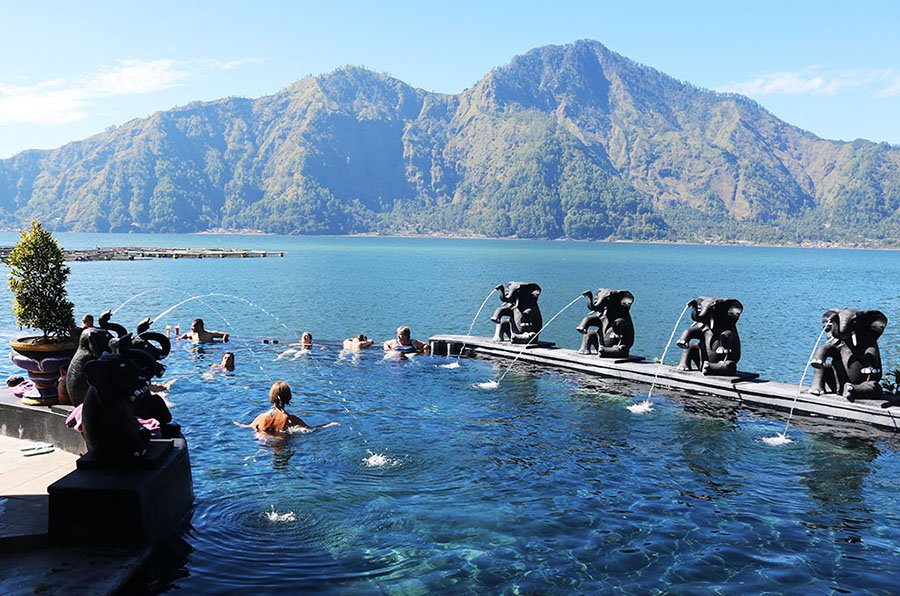 Tourists relaxing in a natural hot spring pool with a view of the Mount Batur volcano in Kintamani.