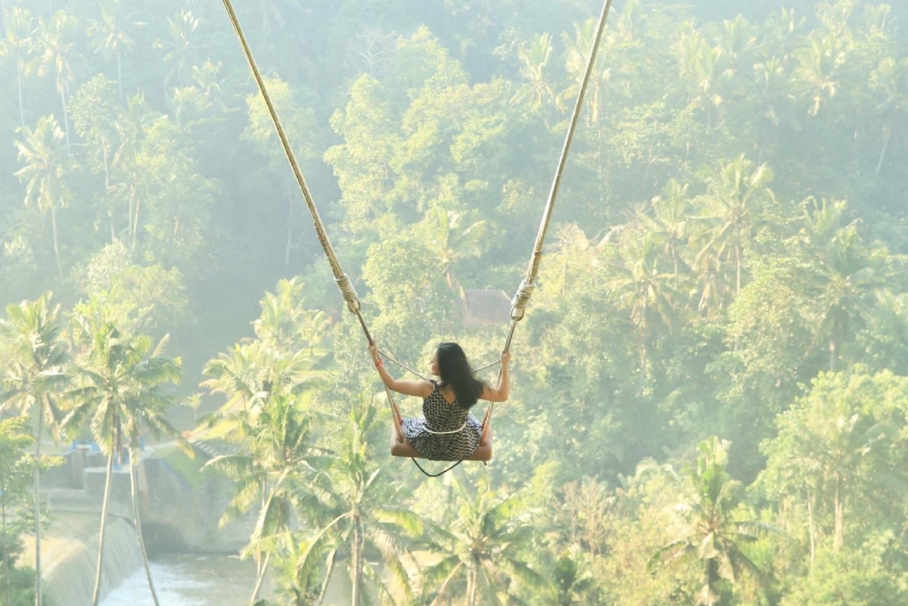 A woman in a long red dress swinging high above a lush green jungle valley on the famous Bali Swing.